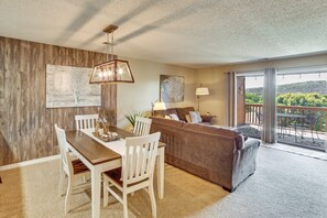 Un espace repas comprenant une table et des chaises en bois, un canapé et un balcon avec vue.