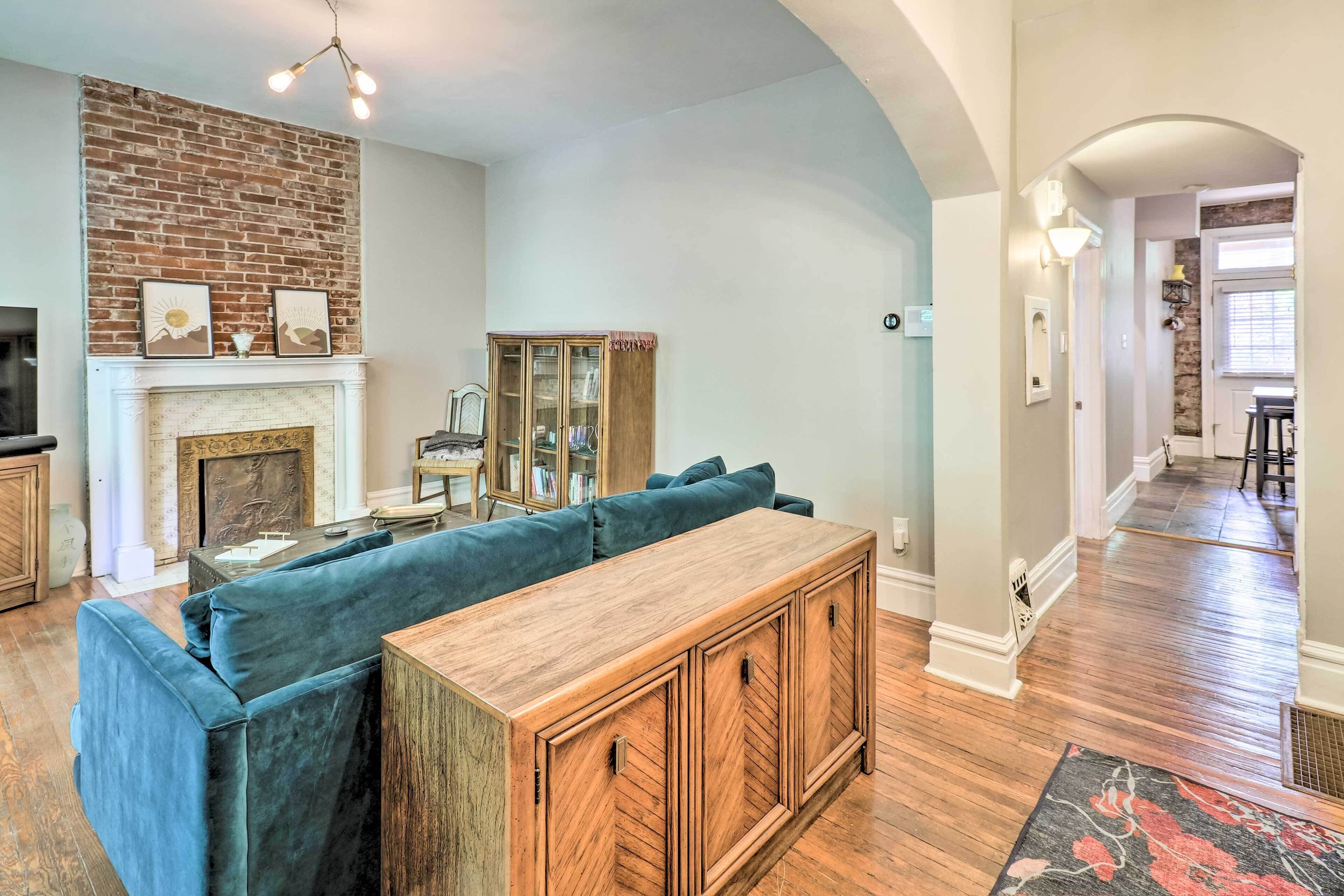 Un salon avec un mur en briques, une cheminée, un canapé bleu et un meuble en bois.
