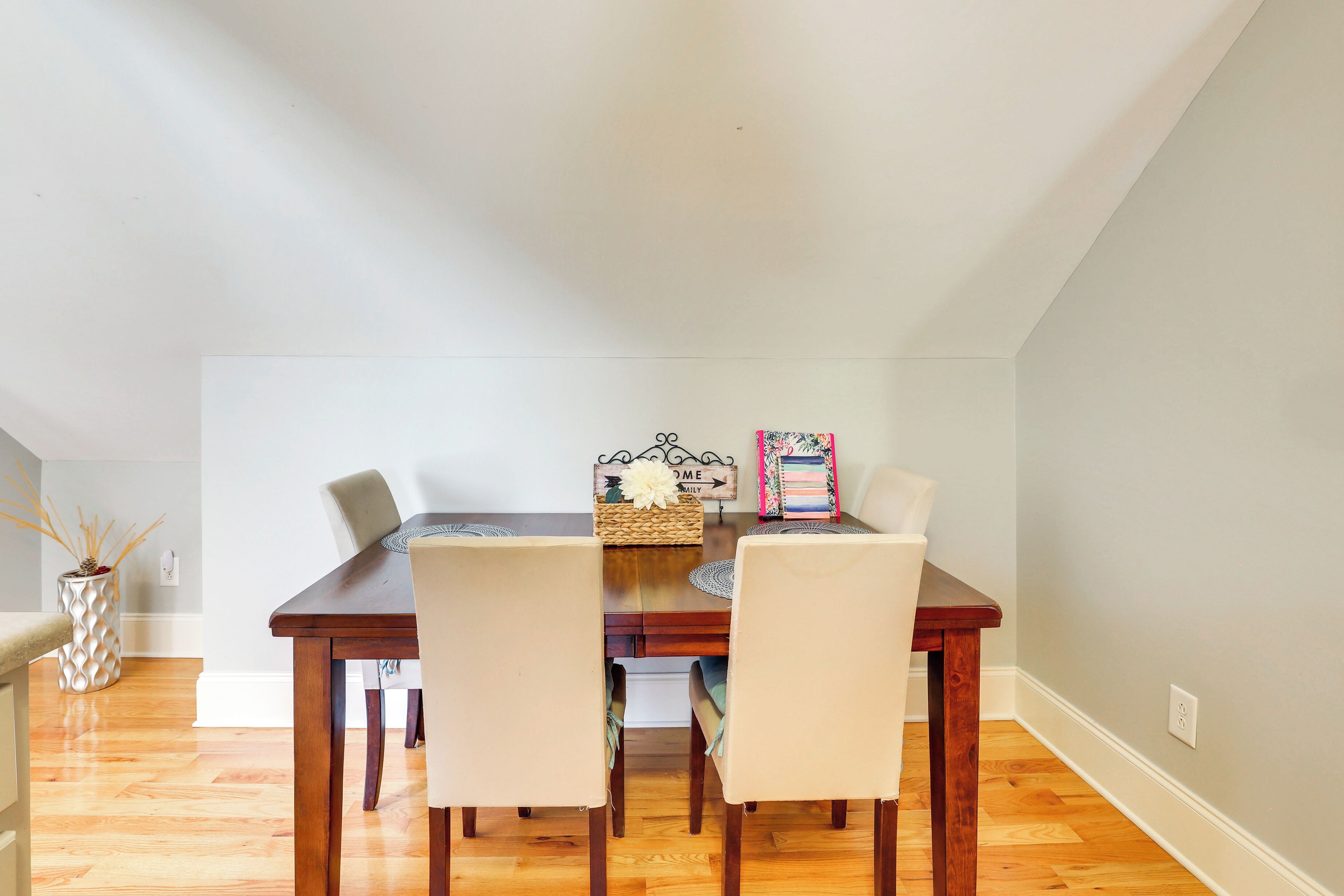A dining area with a wooden table and four chairs, a decorative basket, and a wall-mounted light switch.