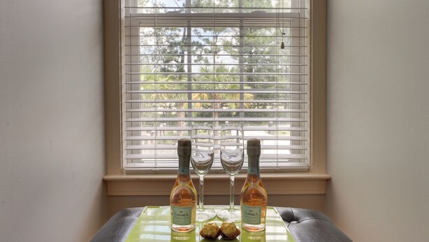 A table with two bottles of wine, two wine glasses, and two chocolates in front of a window with blinds. - 4 Mi to Dtwn: Simplistic Summerville Studio (Summerville)