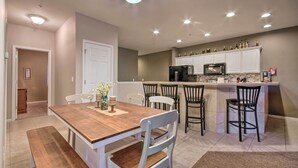 Una cocina moderna con armarios blancos, una isla central con taburetes y un área de comedor con mesa y sillas de madera.