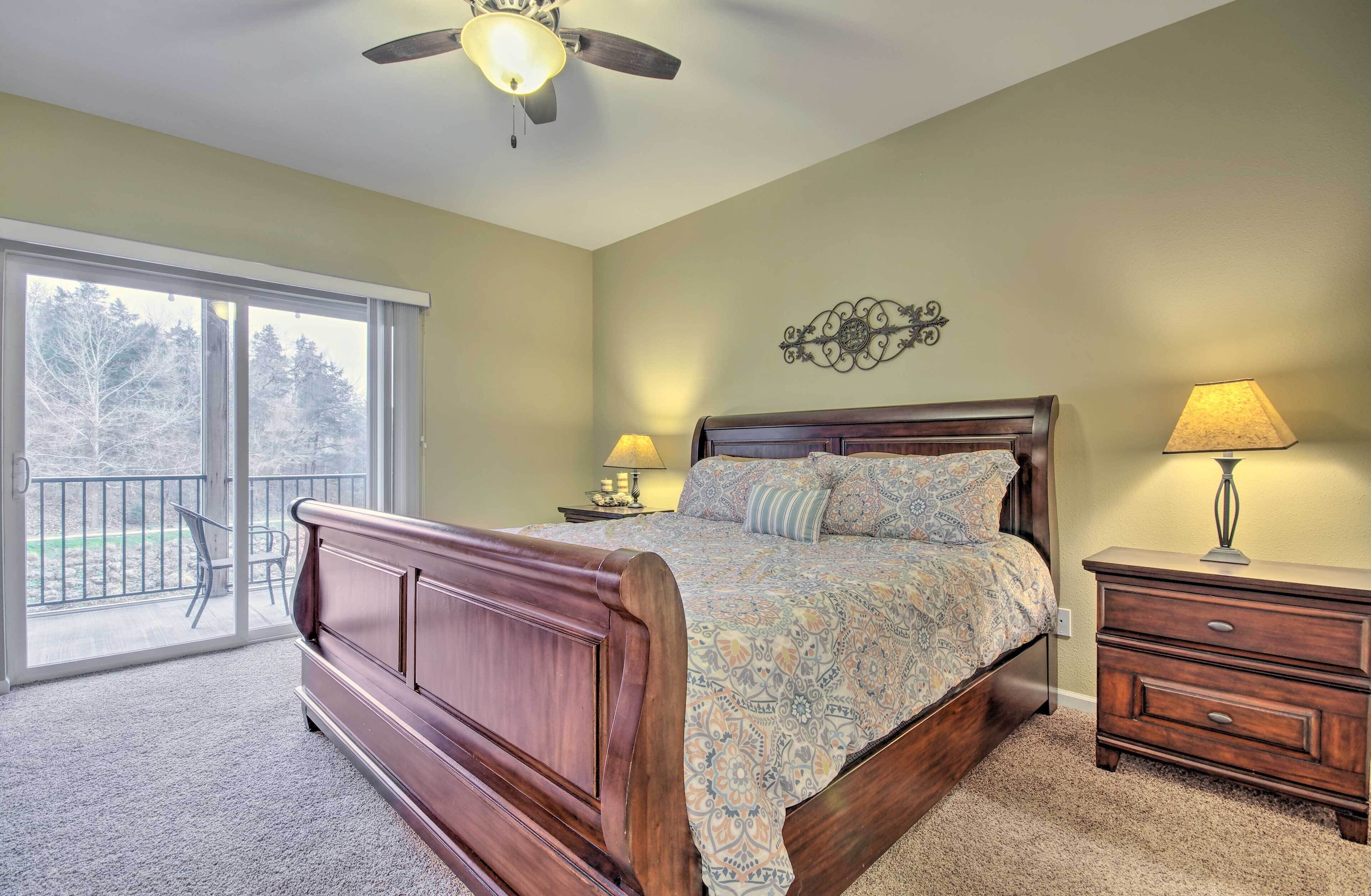 A bedroom with a wooden bed, a ceiling fan, a nightstand with a lamp, and a balcony with a chair.