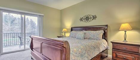 A bedroom with a wooden bed, a ceiling fan, a nightstand with a lamp, and a balcony with a chair.