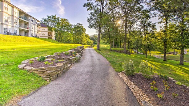 A paved pathway flanked by stone walls and greenery, leading to a building with multiple balconies and a flat roof. - Branson Resort Condo w/ Scenic Patio & Pool Access (Branson)