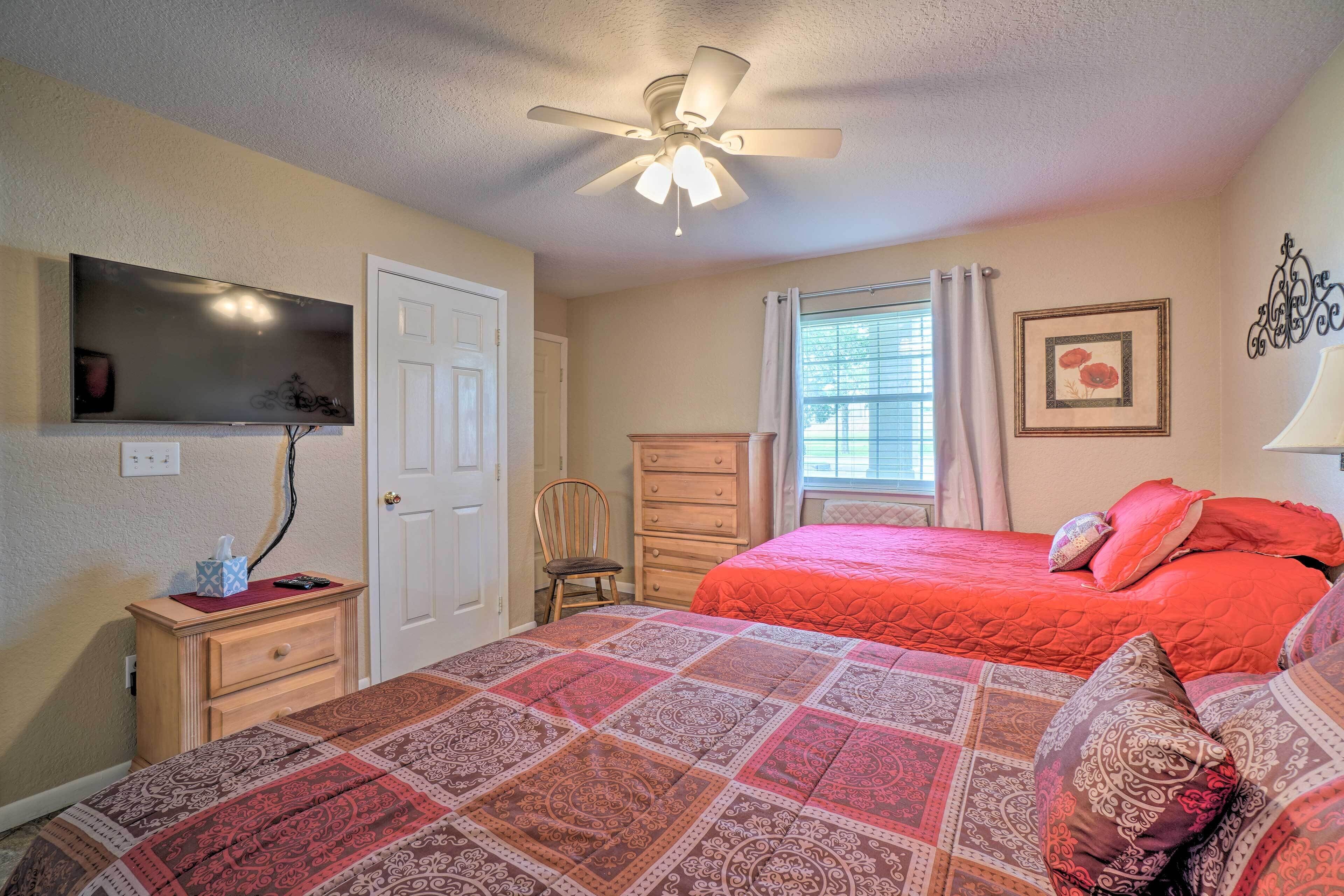A bedroom with a bed, a dresser, a chair, a ceiling fan, a window with curtains, and a wall-mounted TV.