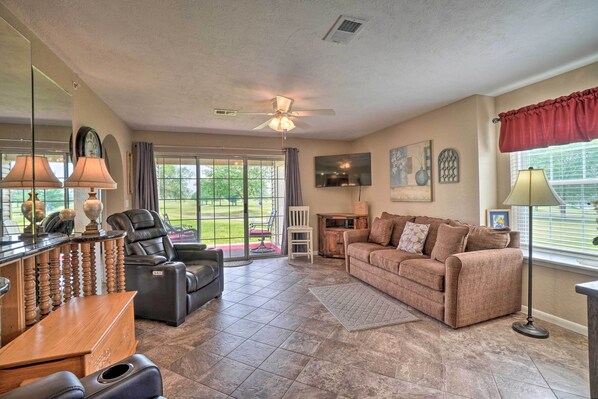 A spacious living room with a leather sofa, a recliner, a wooden coffee table, and a large window with a view of the outdoors.