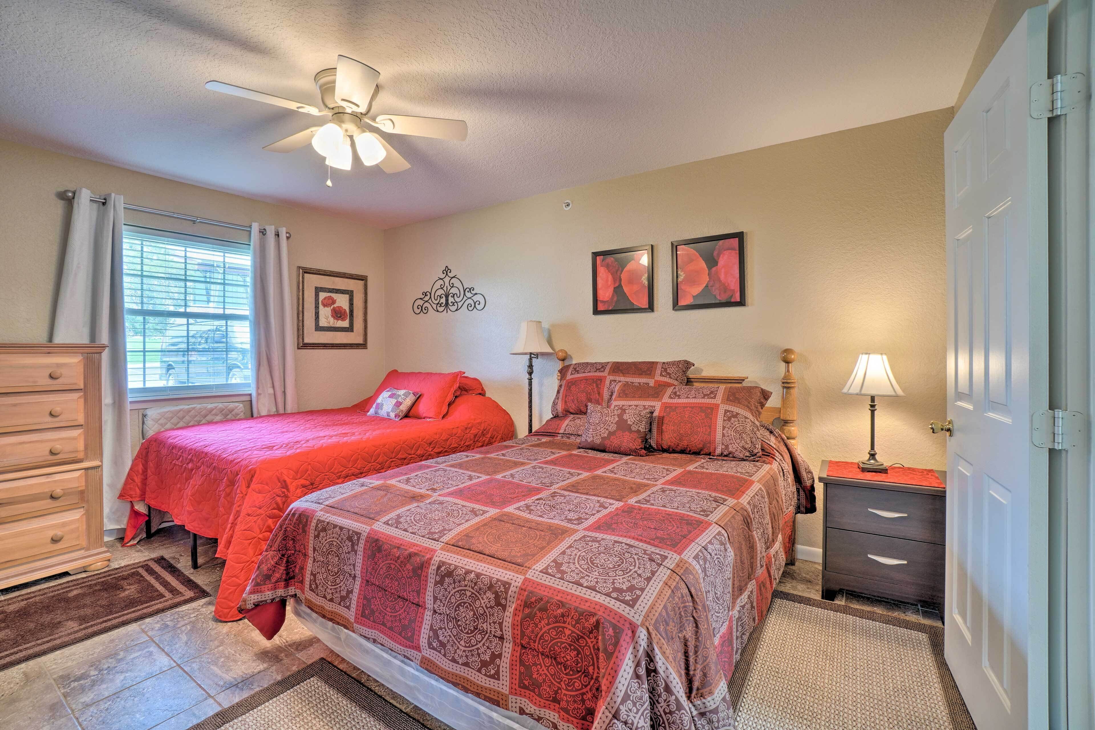 A bedroom with two beds, a ceiling fan, a dresser, and a nightstand with a lamp.