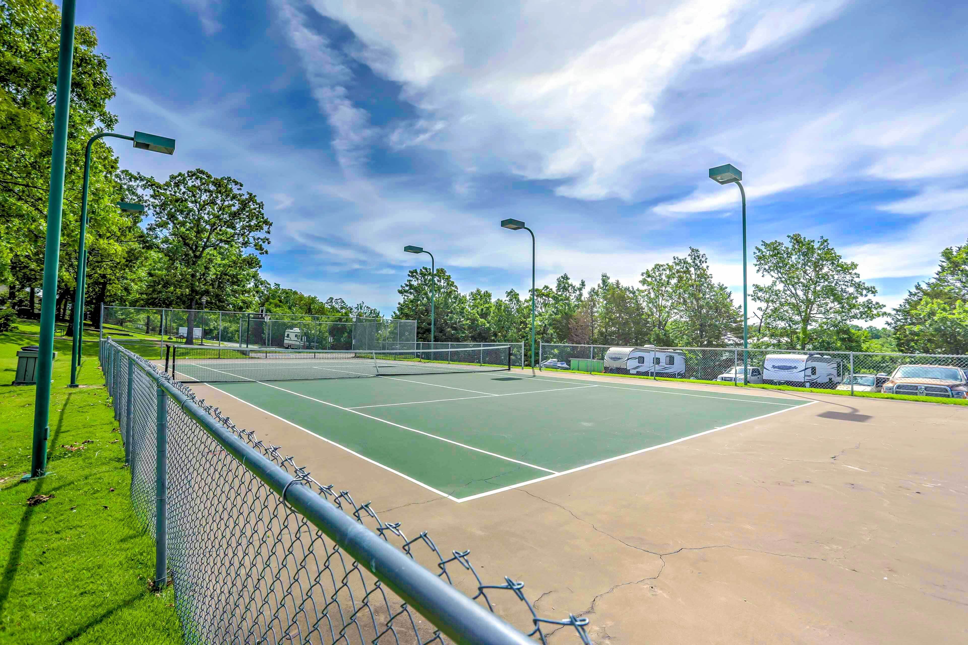 En utomhus tennisbana med ett stängsel av sammanlänkade kedjor, gatlyktor och husbilar parkerade i bakgrunden.