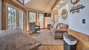 A spacious room with large windows, a wooden ceiling, a sofa, a chair, a table, and a wall clock. - Shell Knob Guest House w/ Lake View, Fire Pit (Shell Knob)