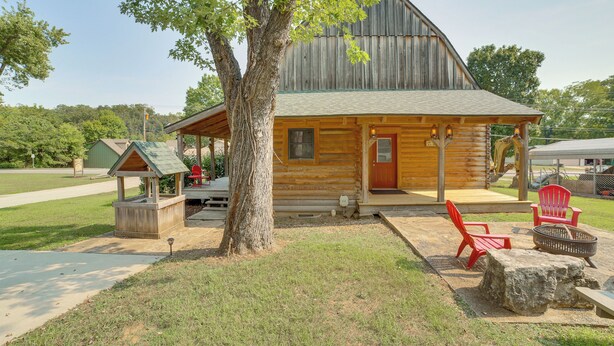 A rustic log cabin with a porch, a small outdoor seating area with red chairs, and a large tree in front. - Rustic Hollister Cabin - 5 Mi to Downtown Branson (Hollister)