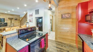 A kitchen with a black stove, granite countertops, wooden walls, and a red refrigerator. - Rustic Hollister Cabin - 5 Mi to Downtown Branson (Hollister)