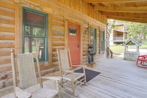 A wooden cabin with a porch, two rocking chairs, a red door, and a small statue. - Rustic Hollister Cabin - 5 Mi to Downtown Branson (Hollister)