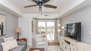A modern living room with a grey sofa, a white armchair, a wooden coffee table, a TV on a wooden cabinet, and a ceiling fan. - Summerhouse Villas Condo: Private Resort Beach! (Pawleys Island)