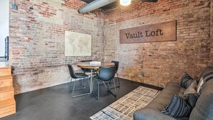 A room with a brick wall, a 'Vault Loft' sign, a round table with chairs, and a sofa with striped pillows. - Sleek, Modern Loft in Downtown Springfield! (Springfield)