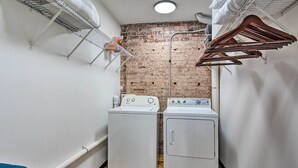 A laundry room with two washing machines, a brick wall, and a wooden floor. - Sleek, Modern Loft in Downtown Springfield! (Springfield)