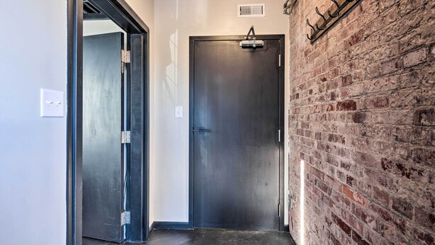 A hallway with a metal door, a brick wall, and a light fixture. - Sleek, Modern Loft in Downtown Springfield! (Springfield)