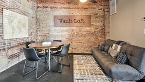 A room with a brick wall, a ceiling fan, a table with chairs, a sofa, and a rug. - Sleek, Modern Loft in Downtown Springfield! (Springfield)