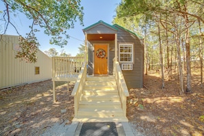 A small wooden cabin with a porch and a door, surrounded by trees.