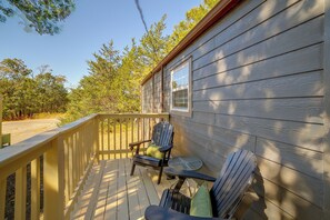 Um deck de madeira com guarda-corpo, uma janela e duas cadeiras Adirondack.