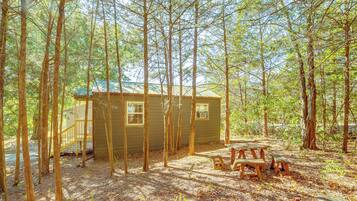 A cabin surrounded by tall trees, with a picnic table and a small deck area.