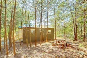 A cabin surrounded by tall trees, with a picnic table and a small deck area.
