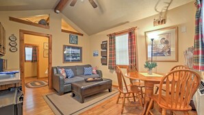 A cozy living room with a gray sofa, wooden dining table, and chairs. There is a kitchen area with a refrigerator and a countertop. - Near Shopping & Museums: Quiet Branson Cabin (Branson)
