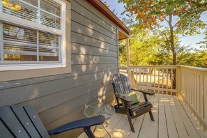Um deck de madeira com uma cadeira e um banco, corrimão e uma casa com revestimento e janelas.
