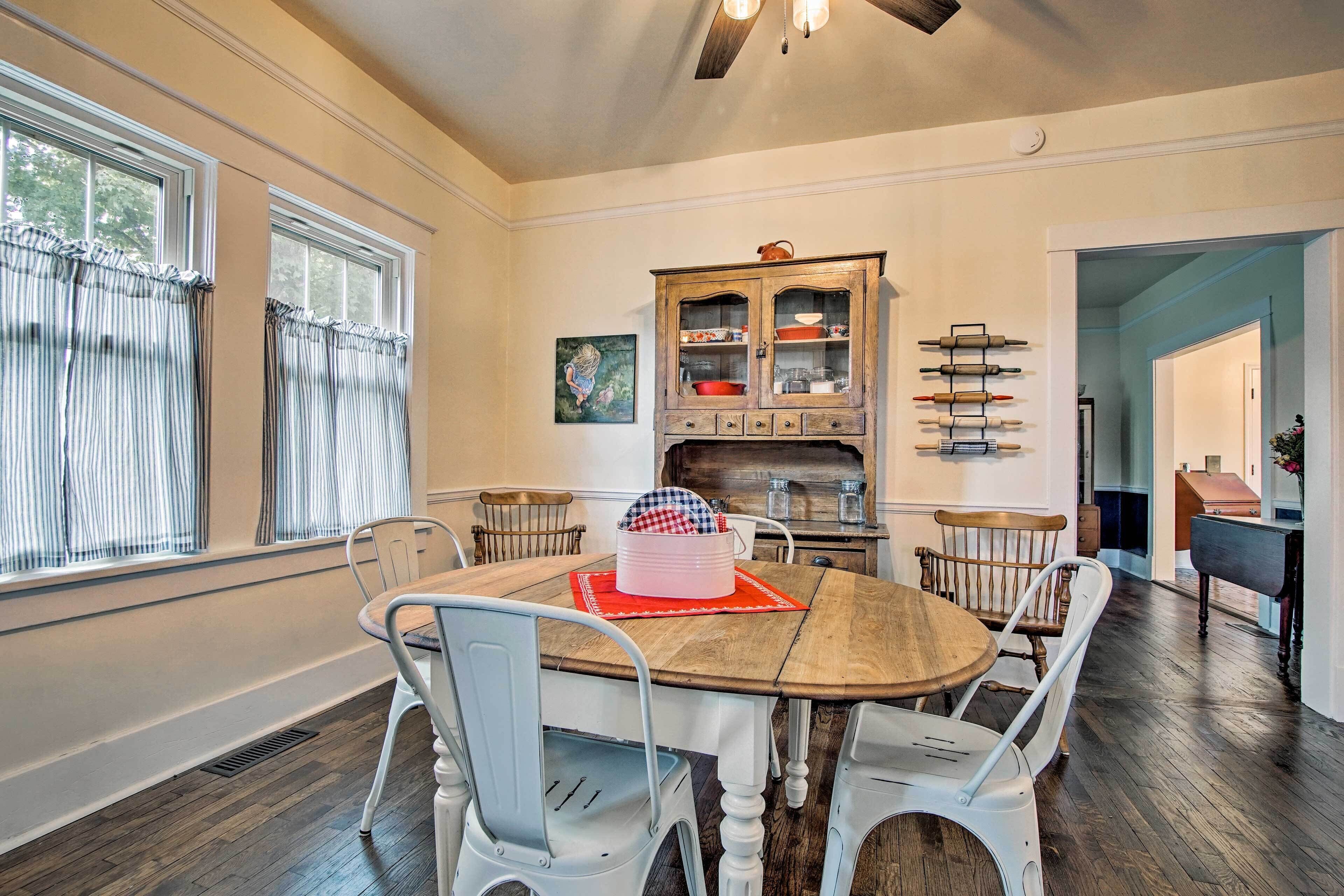 A dining area with a wooden table, white chairs, a cabinet with glass doors, and a painting on the wall.
