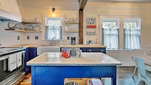 A kitchen with a central island, white tiled walls, wooden beams, and a window with curtains. - Remodeled Historic Farmhouse ~ 20 Mi to KC! (Liberty)