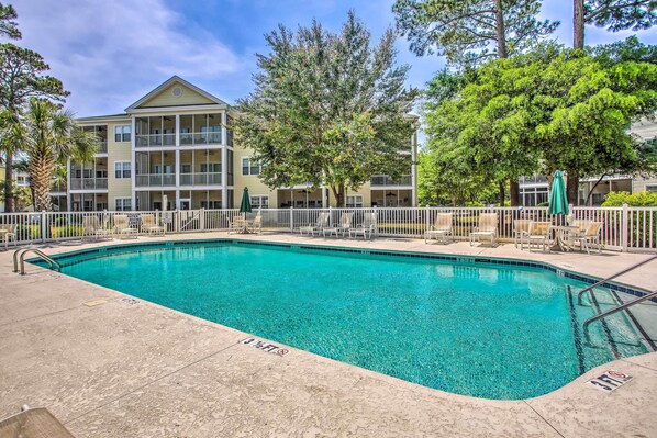 A swimming pool with a 3-foot depth marker, surrounded by a fence, and adjacent to a multi-story building with balconies. - Sunny Coastal Condo ~ 1 Mi to N Myrtle Beach! (North Myrtle Beach)