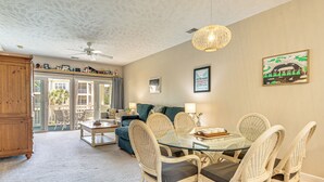 A dining area with a glass table and wicker chairs, a ceiling fan, and a view through glass doors to an outdoor balcony. - Sunny Coastal Condo ~ 1 Mi to N Myrtle Beach! (North Myrtle Beach)
