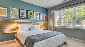 A bedroom with a bed, a window with blinds, and wall art. - Sunny Coastal Condo ~ 1 Mi to N Myrtle Beach! (North Myrtle Beach)