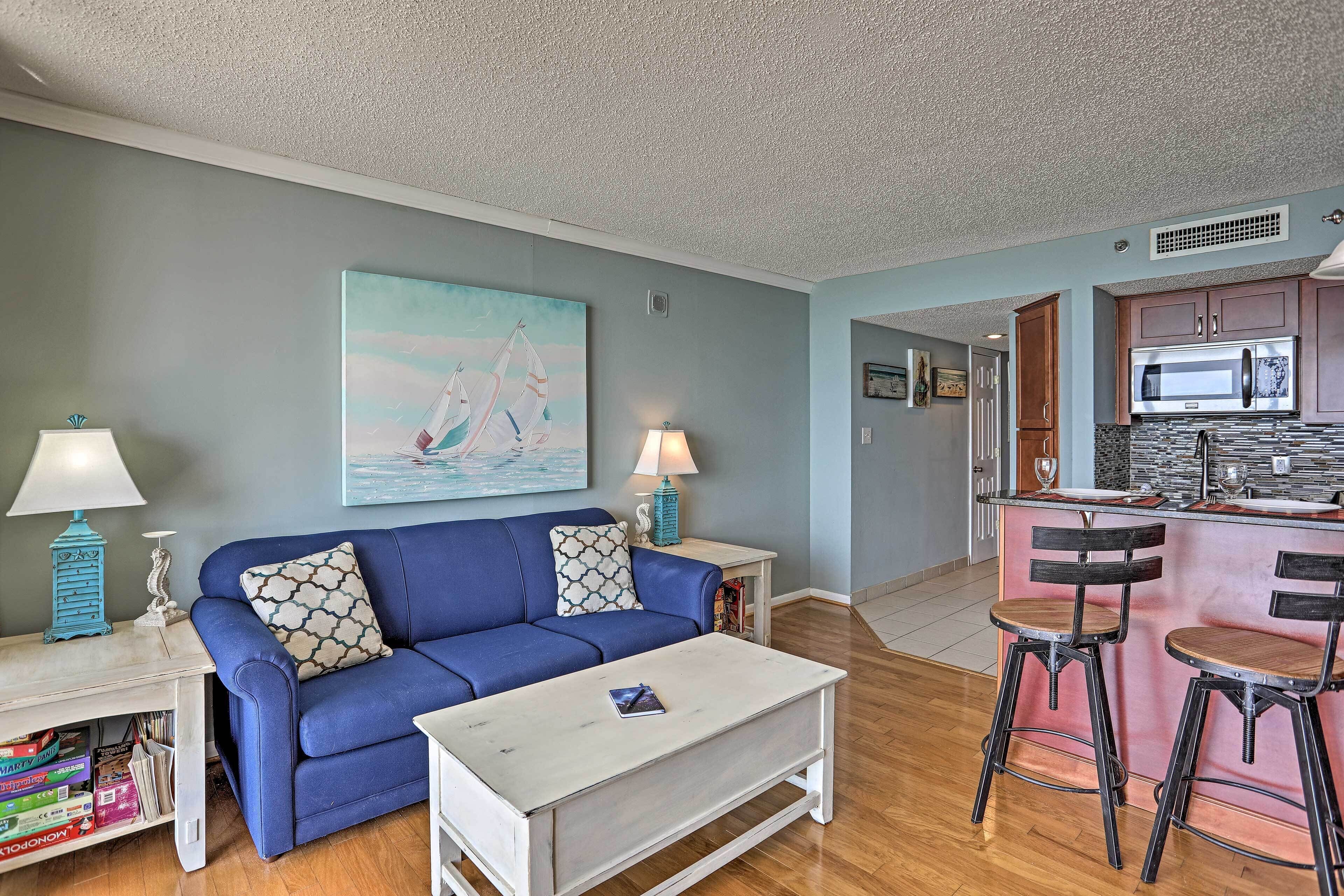 A living room with a blue sofa, white coffee table, and two bar stools.