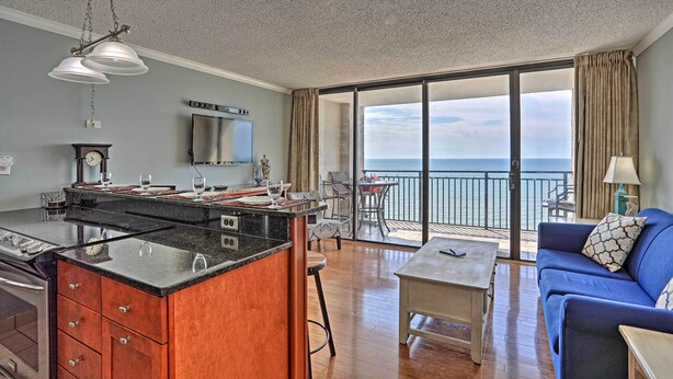 A modern living room with a kitchen, a dining area, and a balcony with a view of the sea. - Community Pool Access: Condo in Myrtle Beach (Myrtle Beach)