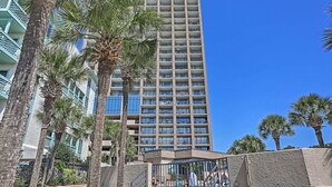 A tall hotel with multiple balconies, surrounded by palm trees and a clear blue sky. - Community Pool Access: Condo in Myrtle Beach (Myrtle Beach)