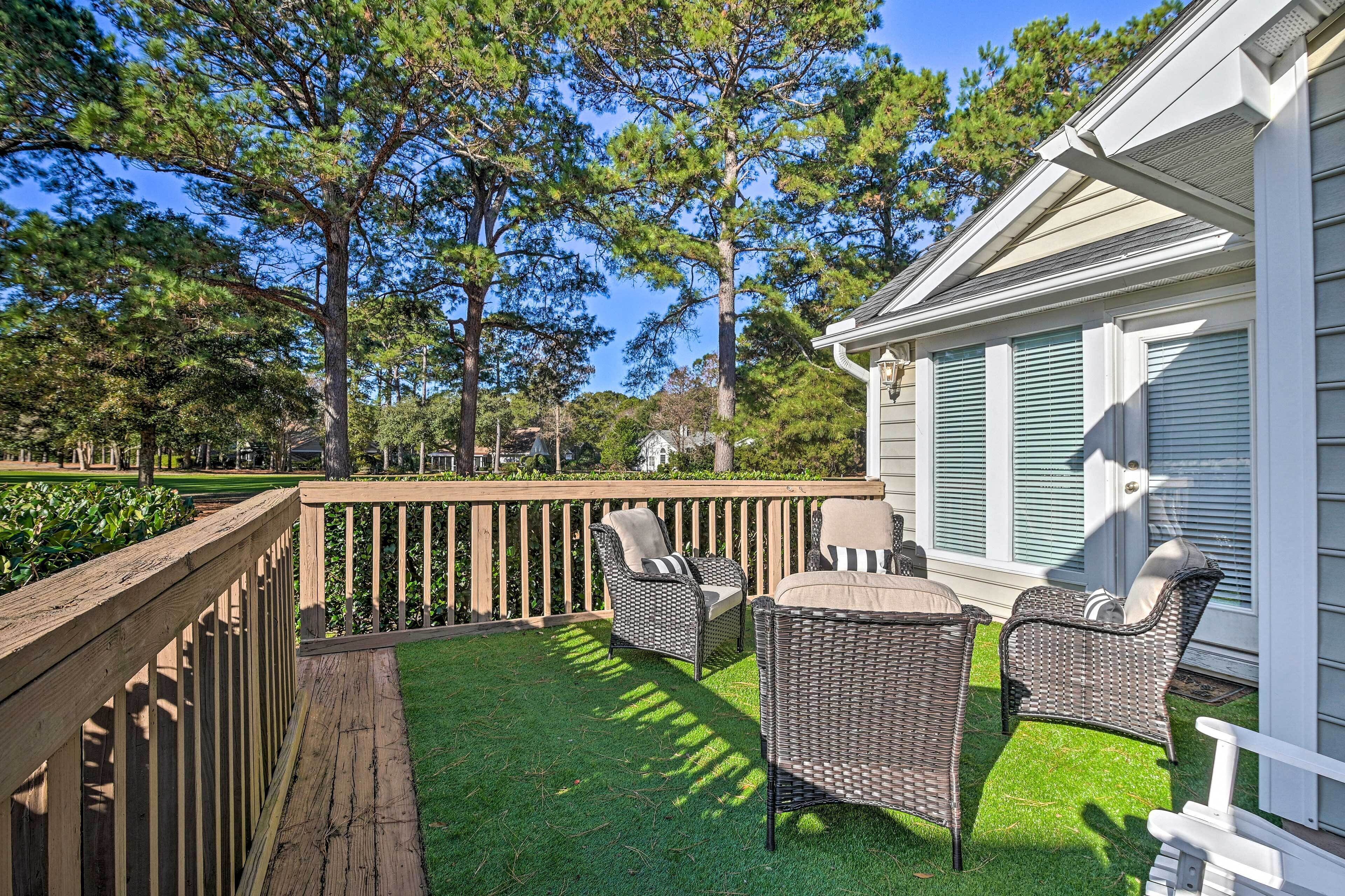 A deck with wicker furniture and a view of trees and a house.