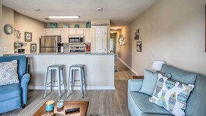 A modern kitchen with a central island, bar stools, and a dining area with a blue sofa and a coffee table. - Sunny N Myrtle Condo w/ Pool < 2 Mi to Beach! (North Myrtle Beach)