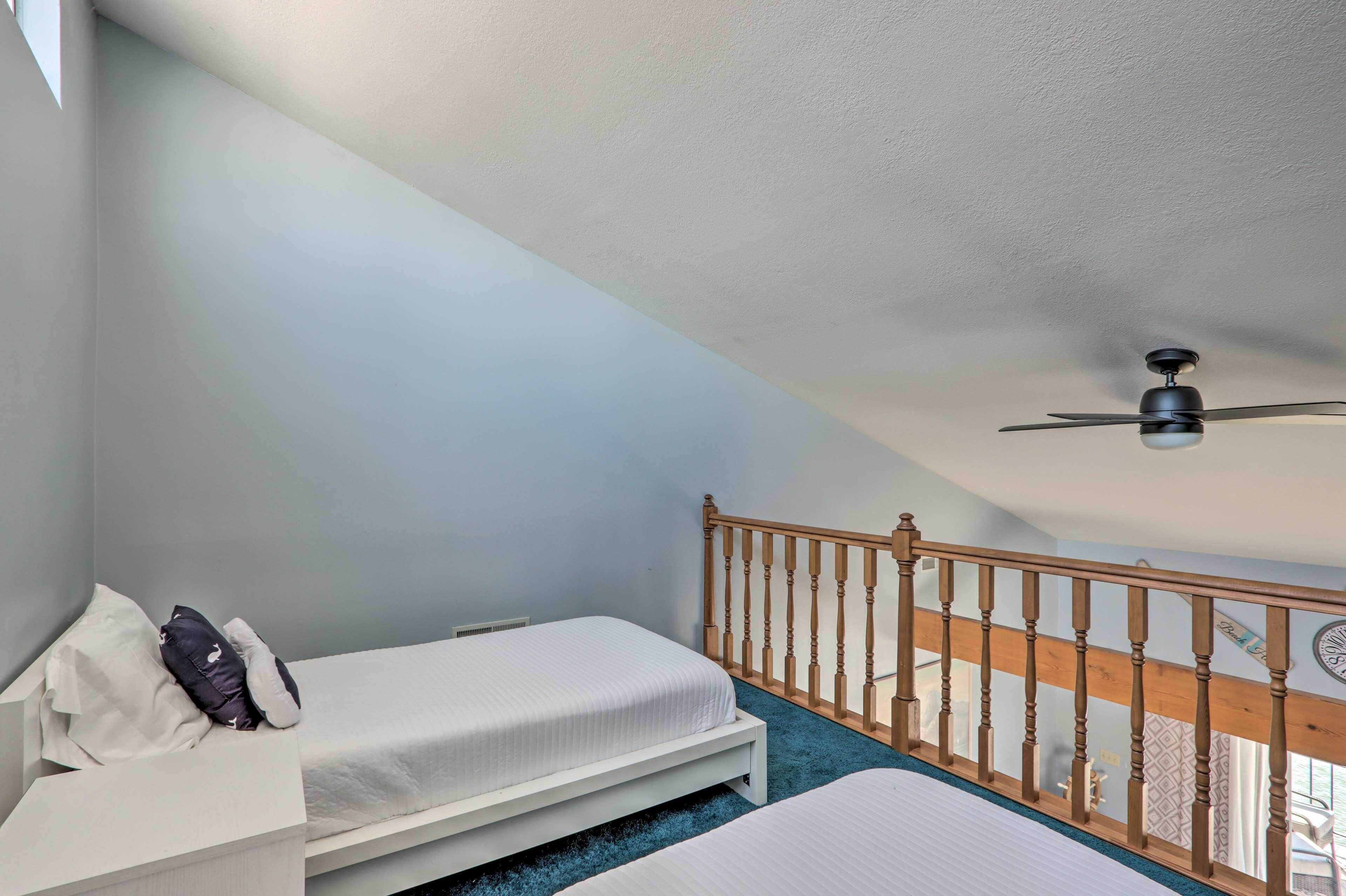 A bedroom with two beds, a ceiling fan, and a wooden railing.