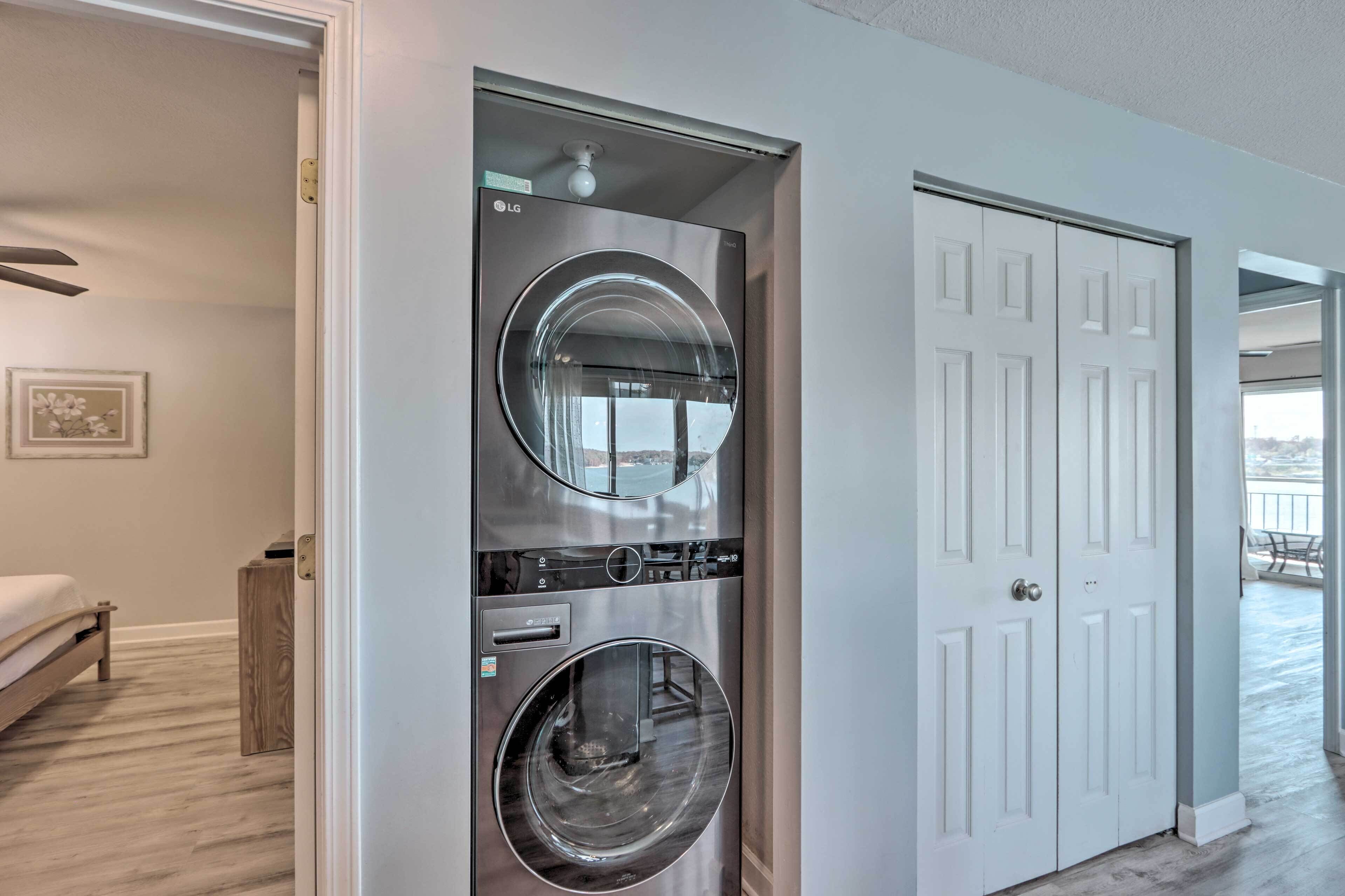A laundry room with two stacked washers and dryers, a wooden bench, and a door leading to a balcony.