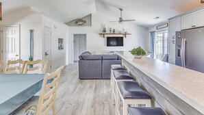Une cuisine moderne dotée d’un four encastré, un coin repas avec une table et des chaises, et un grand canapé d’angle gris.