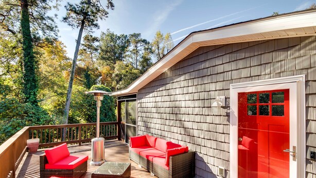 Une terrasse extérieure couverte, aménagée avec des meubles en osier et dotée d’une porte rouge.