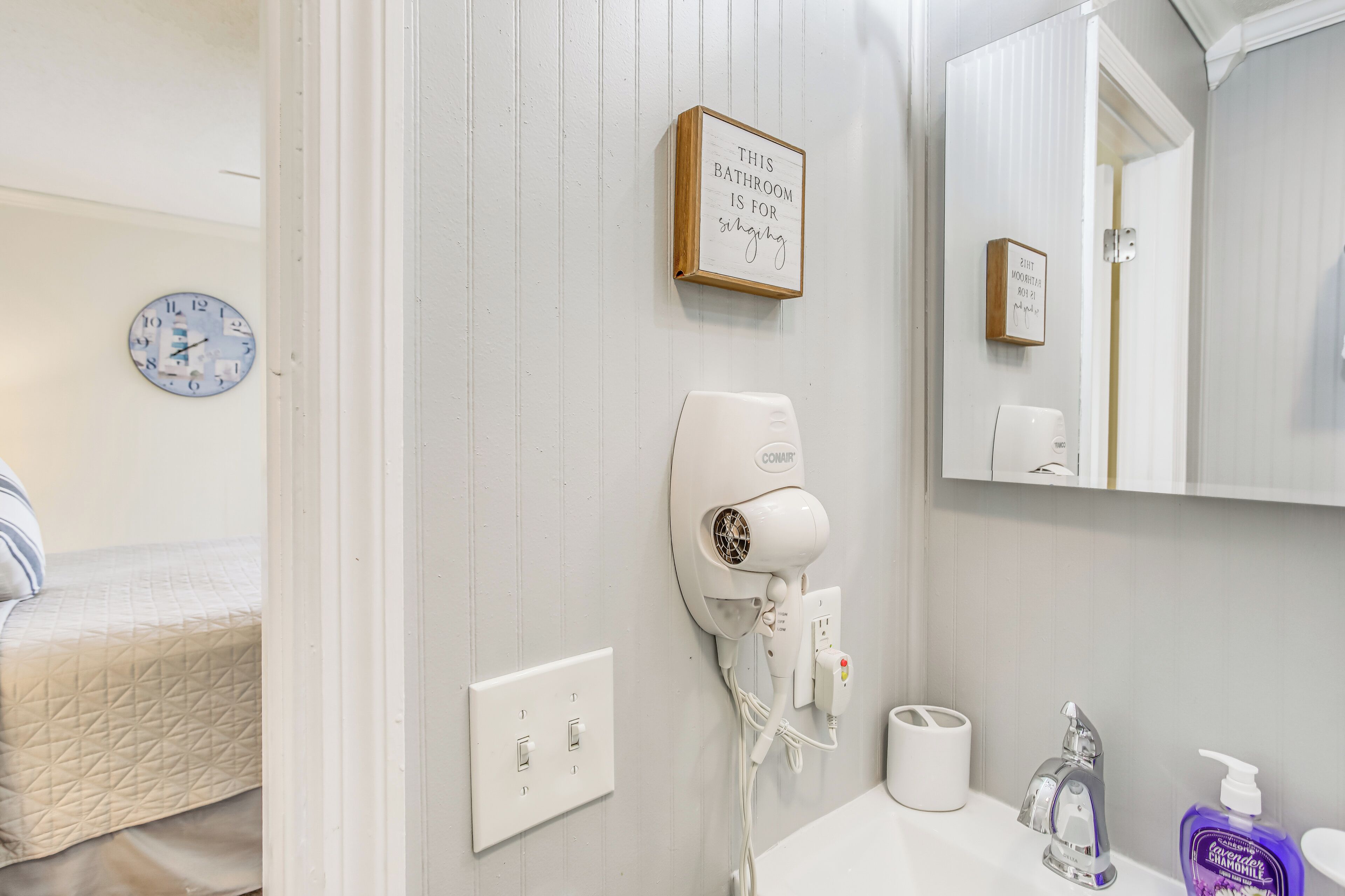 A bathroom with a hairdryer, a clock, and a sign stating "This bathroom is for singing."