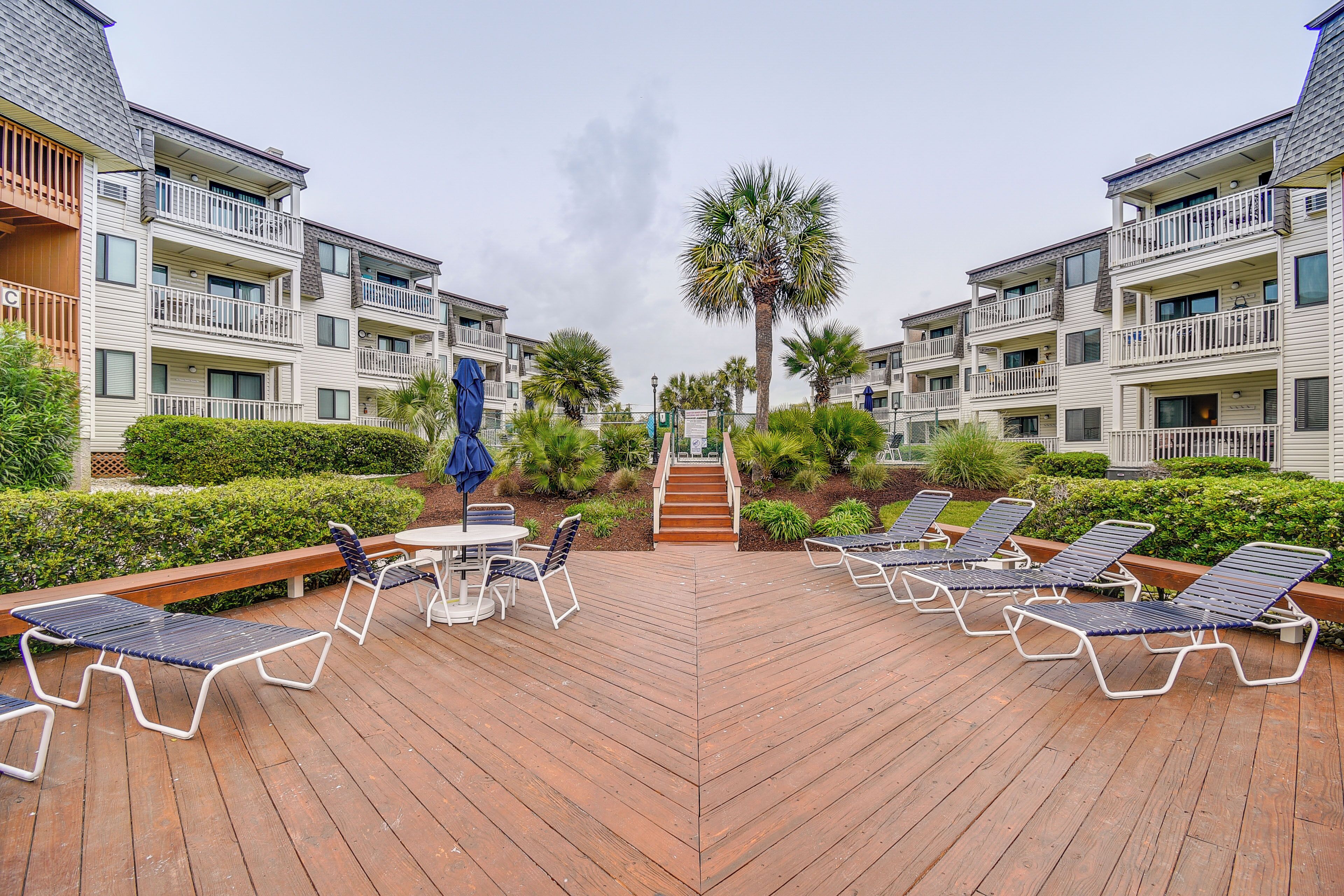 A deck with lounge chairs and a table, surrounded by greenery and a palm tree.