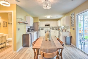 A modern kitchen with white cabinets, a stainless steel refrigerator, and a dining area with a large woven table and chairs.