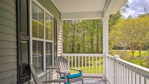 A covered porch with two Adirondack chairs, a small table, and a view of a green landscape. - Summerville Family Home ~ 20 Mi to Charleston (Summerville)
