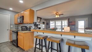 A modern kitchen with wooden cabinets, a stainless steel refrigerator, a built-in oven, a coffee maker, and a large window with a view. - Table Rock Lake Home - Fire Pit & Lake Views! (Golden)