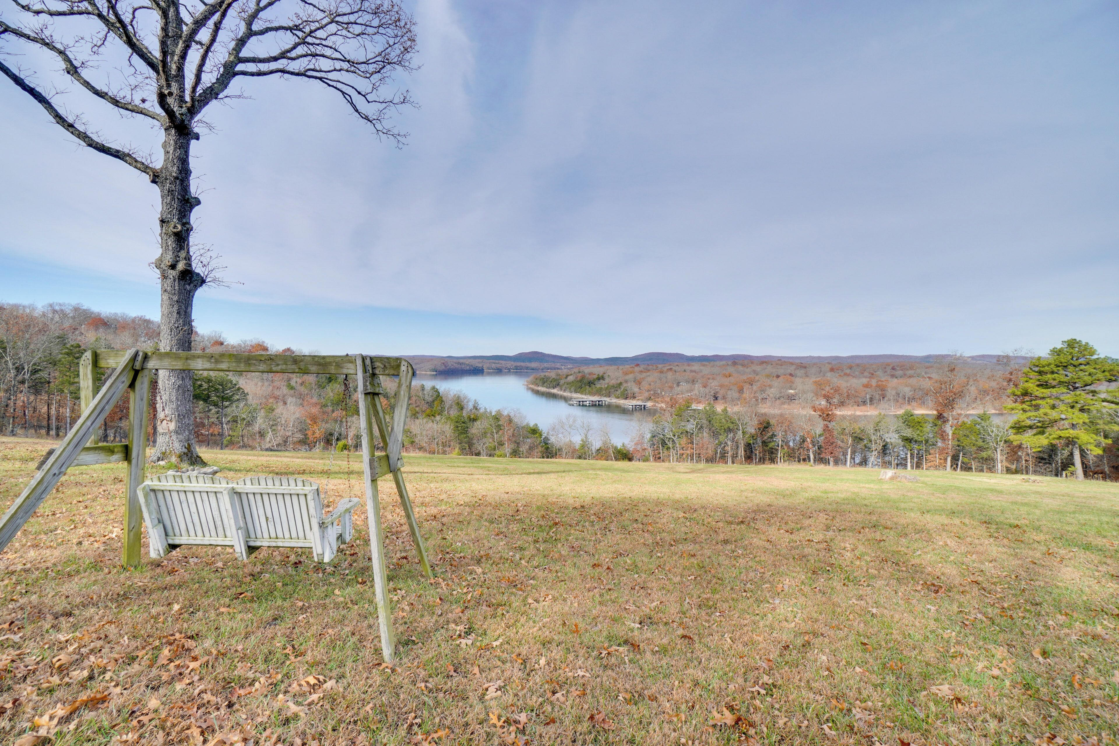A wooden swing set in a grassy area with a view of a river and hills in the background.