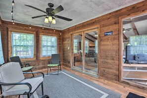 A wooden cabin interior with a ceiling fan, two windows with curtains, a sign reading "Biergarten," and a seating area with chairs and a rug. - Table Rock Lake Getaway w/ Fire Pit, Deck & Grill! (Golden)