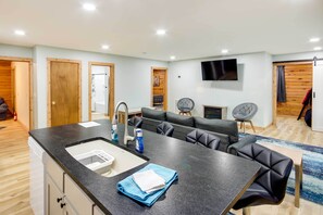A modern kitchen with a black countertop, a sink, and a dining area with a table and chairs. - Tranquil Creekside Hideout: Families Welcome! (Pineville)