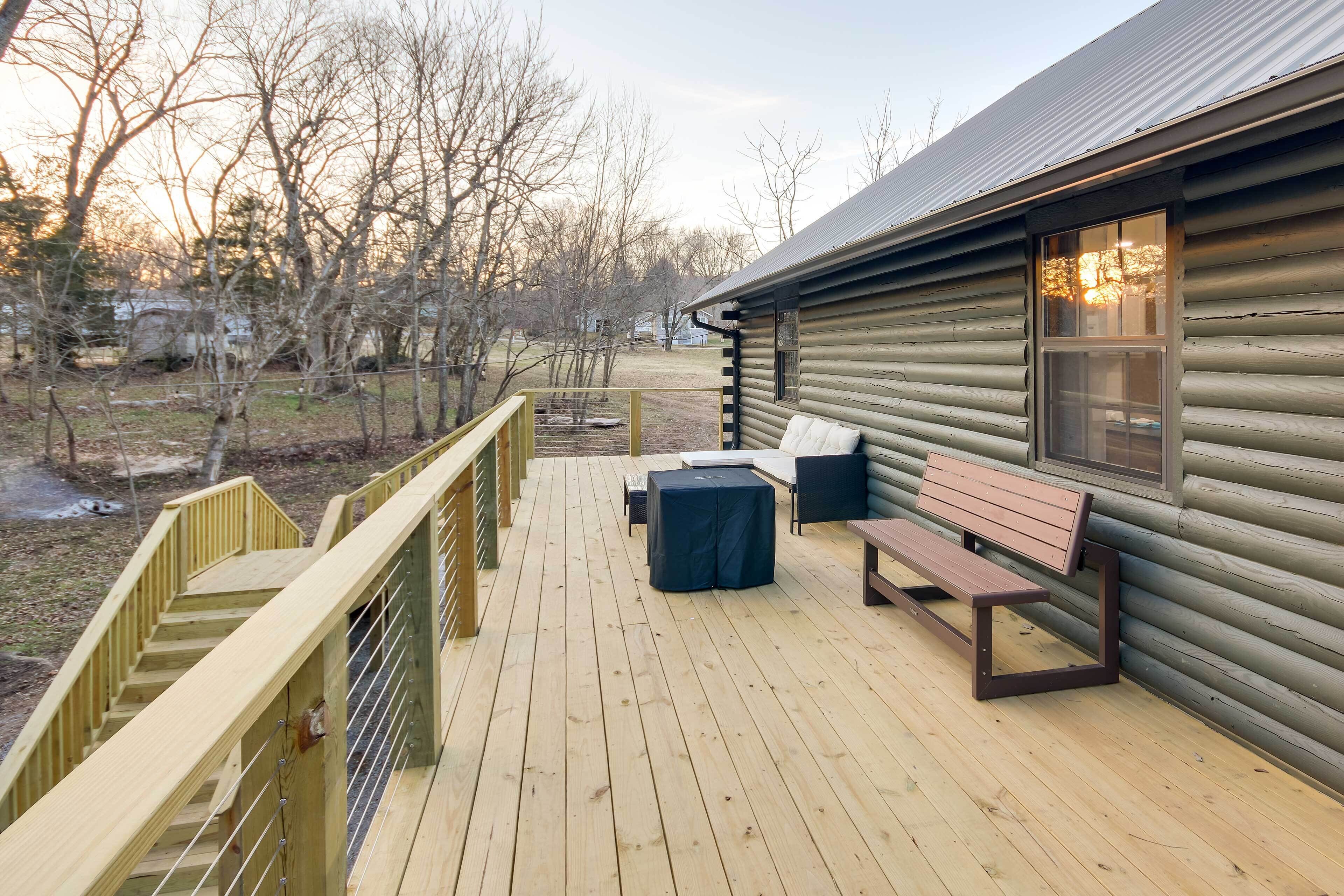 A wooden deck with a bench and table, a railing, and a log cabin in the background.